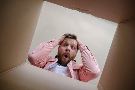 Shocked man found the wrong order in an unpacked delivered box, he is upset and grabs head with own hands. Unboxing inside view.の写真素材