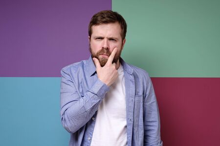 Pensive attractive bearded man with a suspicious look holds hand on face.の写真素材