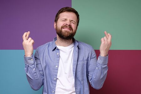 Cute Caucasian man really wants the wish to come true, he crossed fingers and dreamily closed eyes.の写真素材
