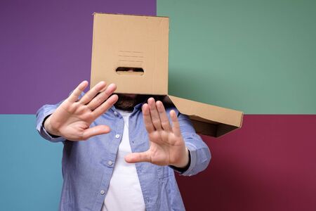 Weird, scared man with a box on his head makes a stop gesture. Concept of fear of society and...