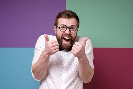 Weird, cheerful man in round glasses makes an approving gesture with hands, thumbs up with a funny grimace on face.の写真素材