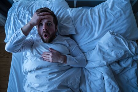 Man had a terrible nightmare, he woke up and looked scared with big eyes. Concept of insomnia and mental health.の写真素材