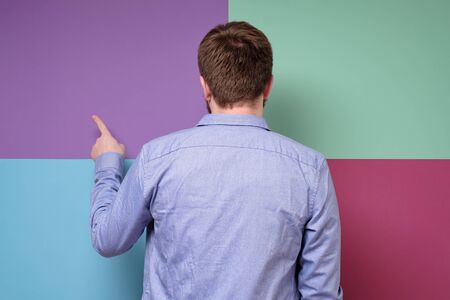 Man in a blue shirt stands with back to the camera and points index finger at the copy space.の写真素材