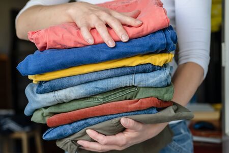 Female hands hold neatly folded trousers and jeans in bright colors, after washing, on a blurred background.の写真素材