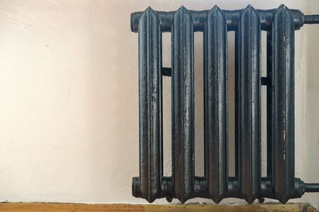 Old cast-iron radiator painted black against a white wall. Copy space.の写真素材