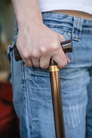 Hand of a young woman with a cane who is temporarily forced to walk and lean on it after a sports injury.の写真素材