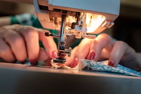 Female hands sew a protective mask using a modern electric sewing machine. Concept of safety during...