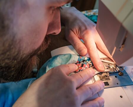 Hands of a concentrated man sew a protective mask using a modern electric sewing machine. Concept of safety during a epidemic.の写真素材