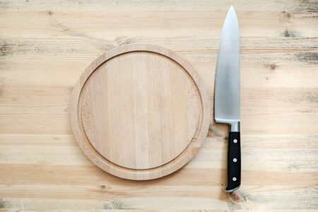 Large sharp knife and a round, wooden cutting board on a table in the kitchen. Copy space. Top view.の写真素材