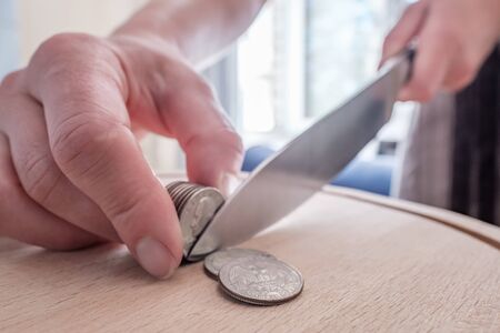 Hands cut dollar coins with a knife, separating them like pieces of food on a cutting board. Concept of taxes, fraud or profit.の写真素材
