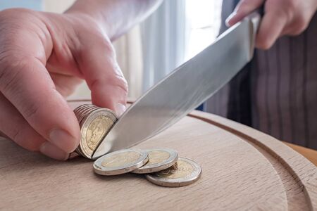 Hands cut euro coins with a knife, separating them like pieces of food, on a cutting board. Concept of taxes, fraud or profit.の写真素材