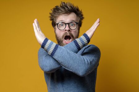 Frightened man shows gesture closed path with arms crossed. Disheveled, displeased hipster makes a stop gesture with hands.の写真素材