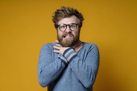 Man with disheveled hair and a beard is under stress, he is crazy, suffocating himself with hands while squeezing neck.の写真素材