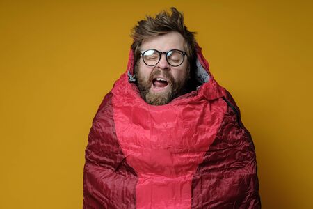 Funny, yawning man in a sleeping bag on a yellow background, he sleeps and imaginary himself in a wonderful travel.の写真素材