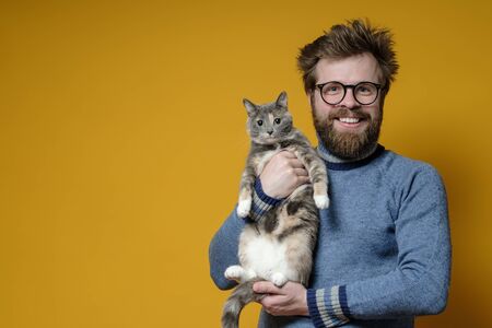 Shaggy, happy man with glasses hugs his adorable cat. Copy space. Concept of love for pets.