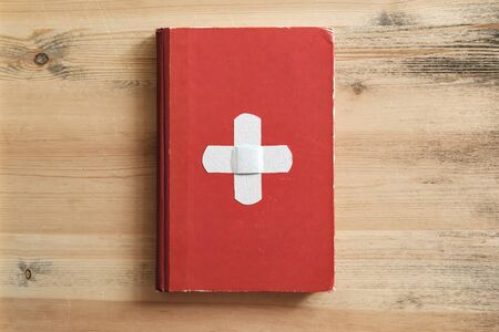 Old red book with a white cross looks like the flag of Switzerland, on a wooden table background. Creative idea. Top view.の写真素材