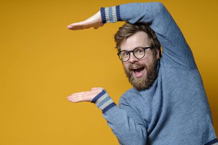 Funny man shows using some size, standing in an unusual pose and smiles joyfully while looking at the camera. Copy space.の写真素材
