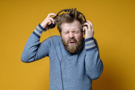 Annoyed hipster in an old sweater takes off headphones, he is unhappy with the music and makes an indignant grimace on face.の写真素材