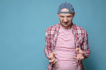 Angry man in a cap and casual clothes looks furiously and makes a gesture with his hands. Copy...