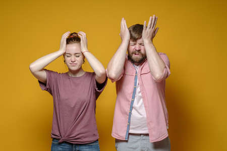 Man and a woman suffer from headaches, they hold their heads with their hands, closing their eyes. Health concept.の写真素材