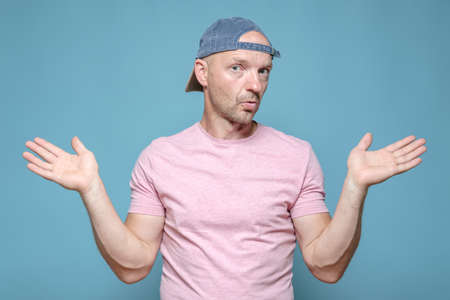 Man with an innocent expression on face spreads arms to the sides and looks at the camera in bewilderment. Blue background.の写真素材
