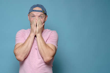 Man is shocked by a pleasant surprise, he covers mouth with hands in amazement and looks at the camera. Copy space.の写真素材