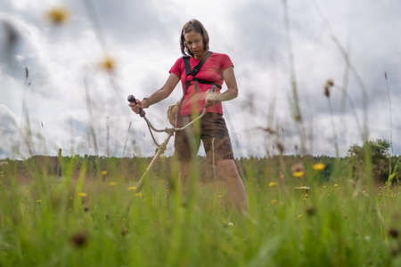 Woman farmer with a petrol trimmer mows the grass in the backyard of the village. Life in the...
