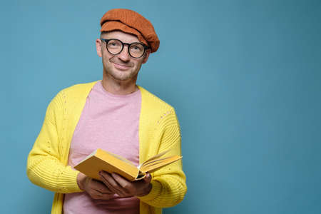 Smiling man in bright clothes, holding an open book in hands and looking at the camera. Funny creative person. Copy space.の写真素材