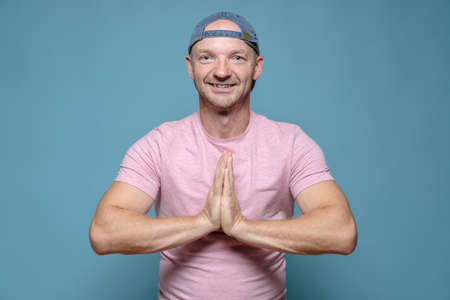 Benevolent, smiling man folded hands in a namaste gesture. Blue background.の写真素材