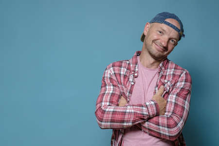 Cute, smiling man stands with crossed arms. Copy space. Blue background.の写真素材