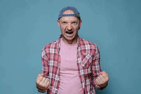 Caucasian man threatens someone, he clenched his fists showing his strength and shouts furiously. Blue background.の写真素材