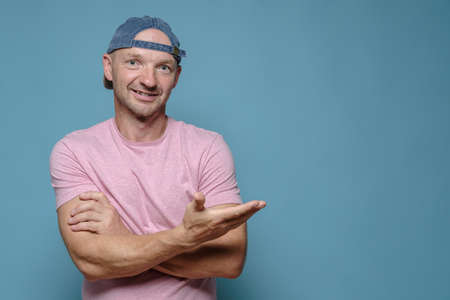 Attractive, smiling man with crossed arms invites somewhere by making a hand gesture. Copy space.の写真素材