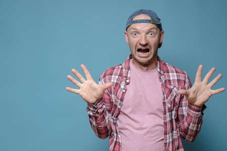 Shocked man in a cap and shirt made a gesture with hands, he screams loudly in surprise and looks with big eyes. Copy space.の写真素材