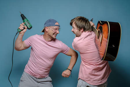 Furious musician and construction worker, they started a fight over the noise, one threatens with a drill, the other with a guitar.の写真素材