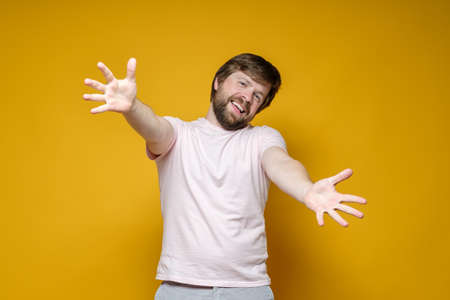Joyful, smiling bearded man stretches his arms for a hug. Welcome. Yellow background.の写真素材