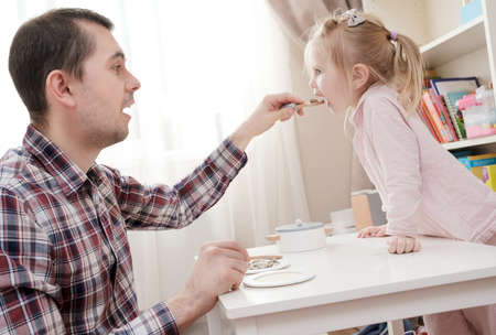 Caring father feeds his lovely daughter with delicious food using a spoon in a cozy home.の写真素材