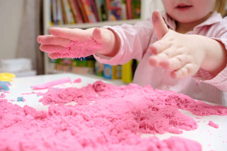 Enthusiastic child is playing with pink kinetic sand. Concept of developing fine motor skills and creative imagination in children.の写真素材