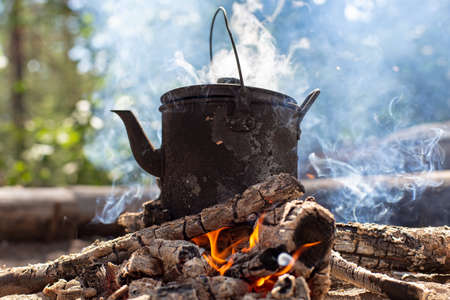 Boiling kettle with hot drink stands on a campfire in the smoke, in a forest.の写真素材