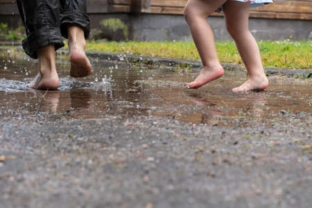 Mother and child are having fun running through the puddles, after the rain in the yard of their house. Lifestyle.の写真素材