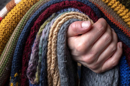 Female hand holding a set of knitted scarf, multi-colored and with different patterns.