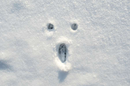 A surprised smiley face painted on the snow, on a sunny winter day. Copy space.