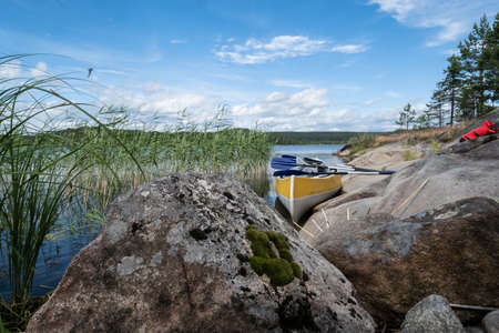 Beautiful landscape. Canoe parked on the sandy shore of the lake, with large stones, on a summer day. Lifestyle.の写真素材