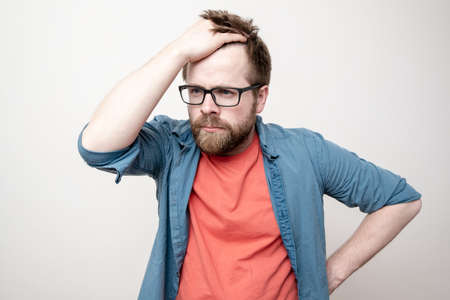 Shocked man holds his hair with hand and looks thoughtfully. White background.