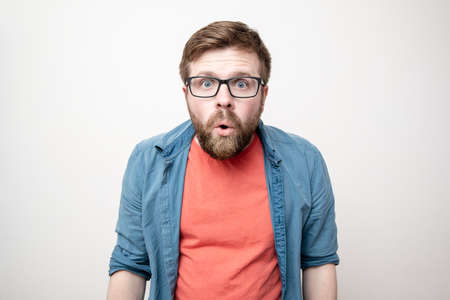 Man in glasses looks in surprise at the camera with his mouth open. White background.の写真素材