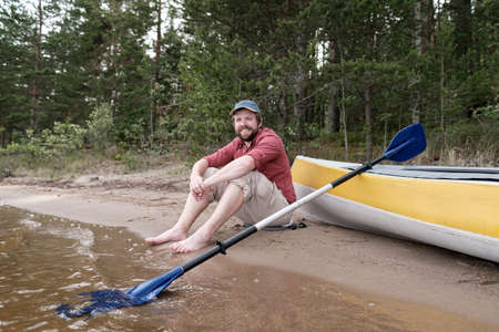 Happy smiling man resting on the shore of the lake after traveling by kayak. Active lifestyle.の写真素材