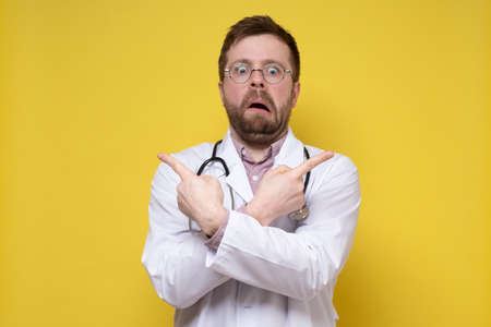 Bizarre, stunned male doctor points index fingers in different directions and looks with a strange expression on face.の写真素材