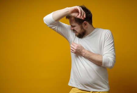 Man in a white t-shirt sniffs his armpits, annoyed by the problem of foul perspiration and body stench. Copy space.の写真素材