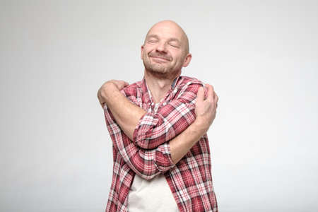 Handsome man in a plaid shirt hugs himself and dreams with his eyes closed. If you feel lonely, hug yourself.の写真素材
