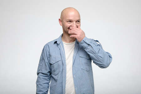 Cheerful bald man looks at someone and laughs, covering mouth with hand.の写真素材