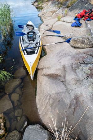 Three-seater kayak with paddles is parked on the rocky shore of the lake, on which life jackets lie. Leisure activities.の写真素材